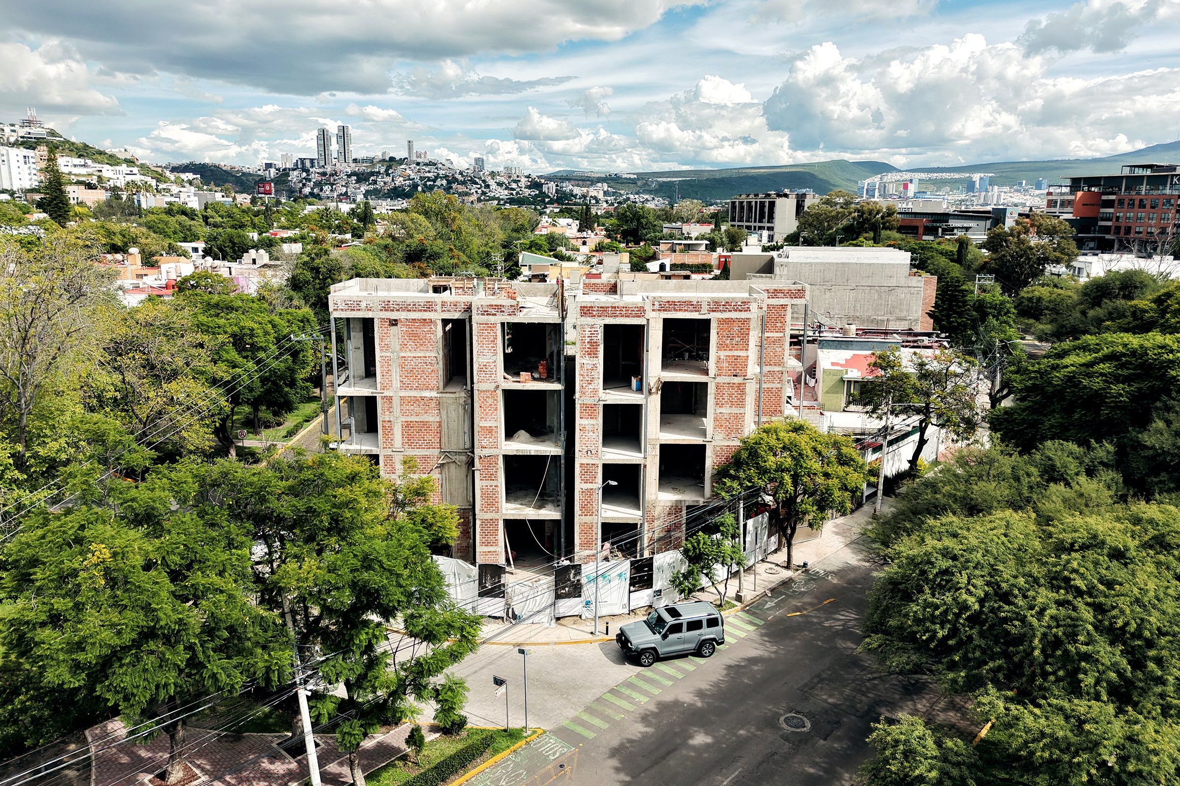 Vista aérea de la esquina con la obra entre los árboles y la sierra al fondo